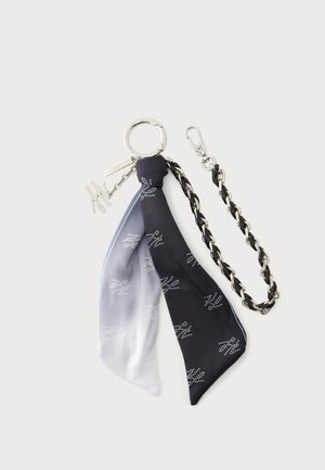 Porte-clés en argent avec chaîne tressée noire et argentée, foulard en soie noir et gris à motifs attaché, et petits charms métalliques décoratifs.
