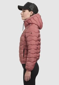 Pink puffer jacket with a hood, featuring a quilted design, elastic cuffs, two side pockets, and black accents, worn with a black cap.