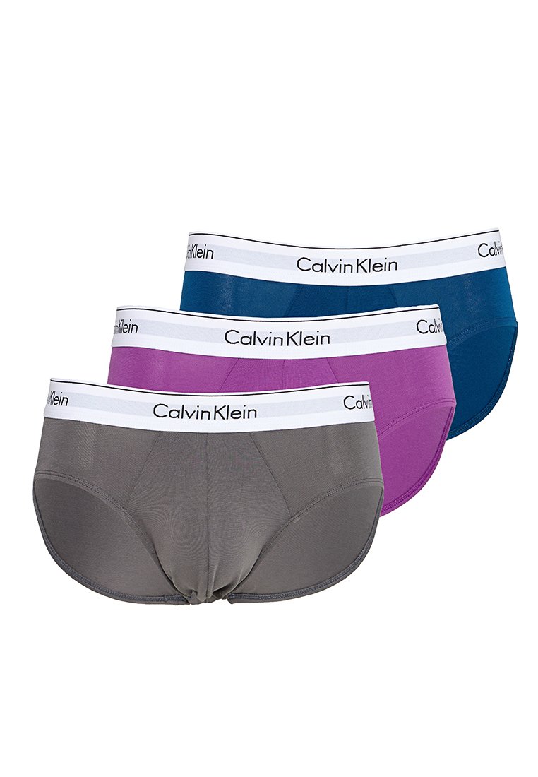 Tres slips de hombre Calvin Klein en gris, púrpura y azul, cada uno con una cinturilla blanca y texto del logo en negro.