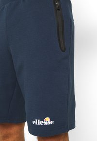 Navy blue shorts made of soft material with a side zip pocket and white logo branding near the hem featuring a colorful emblem.