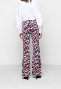 Blouse blanche ajustée associée à un pantalon évasé à motifs comprenant des formes géométriques roses, noires et blanches. Design ajusté avec une texture lisse.