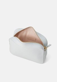 Strukturert hvit lærpung med glidelås, med en rosa innvendig farge og en liten etikett inni. Kompakt, buet design.