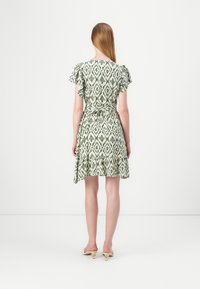 Κοντό πράσινο και λευκό φόρεμα με επαναλαμβανόμενο λουλουδάτο σχέδιο, κοντά φουσκωτά μανίκια, σφιχτή μέση και φουσκωτό στρίφωμα. Φορεμένο με ανοιχτόχρωμα παπούτσια.