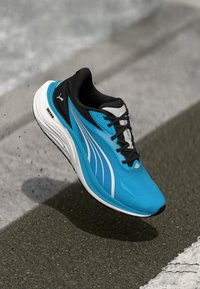 Scarpa da atletica blu con tomaia in rete, dettagli neri, strisce bianche e suola spessa bianca, progettata per l'attività di corsa o allenamento.