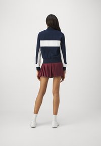 Marinblå och vit kragsjacka med randigt mönster, i kombination med en plommonfärgad plisserad kjol. Vita sportskor fulländar outfiten.