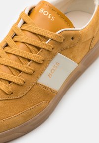 Baskets en daim et cuir jaune moutarde avec lacets assortis, panneau latéral blanc, semelle en gomme et logo "BOSS" sur la languette et sur le côté.