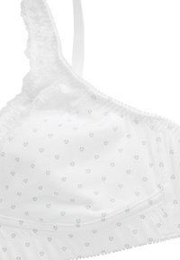 Rintaliivi, jossa on valkoinen pitsireunus ja pieniä sinisiä kukkakuoseja, pehmeä kangas, säädettävät olkaimet ja joustava alaosa tuen tarjoamiseksi.