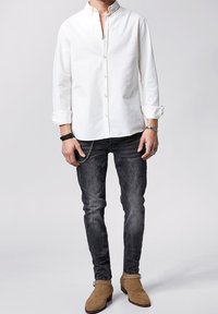 Camicia bianca con bottoni, maniche lunghe, abbinata a jeans scuri e stivali alla caviglia in suede color beige. Dettaglio a catena sui pantaloni. Design semplice e pulito.