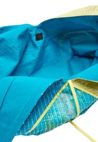 Turkusowe wnętrze torby z teksturowanej tkaniny, z jasnooliwkowymi akcentami i limonkowymi detalami na pasku. Czarna metka widoczna na górze.