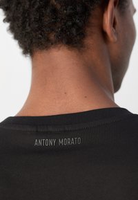 Black t-shirt with a round neckline, featuring a smooth texture and a printed logo “ANTONY MORATO” on the back, just below the collar.