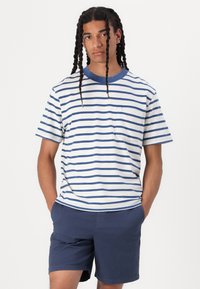 Stribet kortærmet T-shirt i hvid og marineblå, med rund halsudskæring og brystlomme; parret med marineblå shorts. Glat bomuldsstruktur.