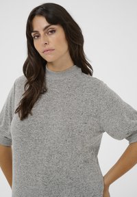 Lyhythihainen vaaleanharmaa paita teksturoidusta kankaasta, korkealla kaula-aukolla ja rennoilla leikkauksilla, jossa on käänteet hihoissa ja sileä pinta.