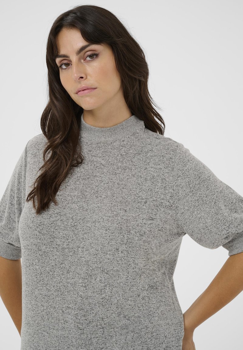 Lyhythihainen vaaleanharmaa paita teksturoidusta kankaasta, korkealla kaula-aukolla ja rennoilla leikkauksilla, jossa on käänteet hihoissa ja sileä pinta.