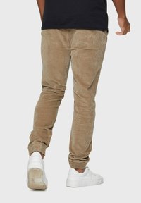 Lichtbruine corduroy broek met tapered benen, elastische boorden en zijzakken, gedragen met witte sneakers. De textuur is ribbelig en zacht.