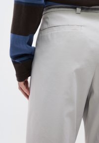Ανοιχτόγκρι παντελόνια με ομαλή υφή, που διαθέτει μία πίσω τσέπη και κομψό σχεδιασμό. Μερικώς ορατό χέρι στη μέση.