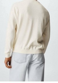 Suéter de algodón crema con puños y dobladillo acanalados, combinado con jeans de mezclilla gris claro que tienen bolsillos traseros. La textura parece suave.