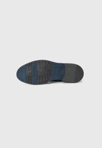 Suela de zapato que presenta material de goma, un inserto azul, patrones de agarre texturizados y una sección de tacón negra y lisa.
