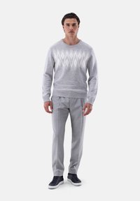 Grau gestrickter Pullover mit Rautenmuster, kombiniert mit hellgrauen karierten Hosen und dunklen Sneakern. Sauberer Schnitt mit gerippten Bündchen und Saum.