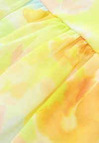 Tissu coloré avec un mélange de motifs floraux jaunes et oranges. Texture légère et légèrement transparente avec des coutures froncées.