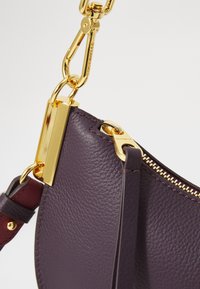 Purple leather handbag with a textured finish, gold-toned hardware, and a zip closure. Features a detachable strap for versatility.