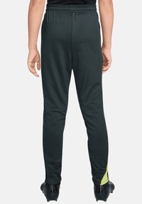 Schwarze Sporthose mit elastischem Bund, verjüngtem Schnitt und gelbem Akzent an der Seite. Hergestellt aus glattem, dehnbarem Stoff.