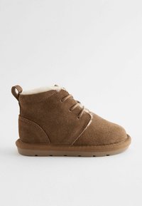Braune Wildleder-Ankle Boots mit Kunstfellfutter, Schnürdesign und flacher Gummisohle. Mit einer kleinen Fersenschlaufe für einfaches Anziehen.