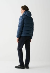 Dunkelblaues Daunenjacke mit Kapuze, mit horizontalen Steppnähten und einer glatten, glänzenden Oberfläche. Kombiniert mit dunklen Hosen und Schuhen.