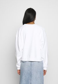 White sweatshirt with a relaxed fit, drop shoulders, ribbed hem, and soft texture. Paired with a light blue denim skirt.