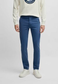 Niebieskie bawełniane spodnie o slim fit. Posiadają zapięcie na guzik z przodu i kieszenie boczne. Noszone z białym swetrem w wzory i trampkami.