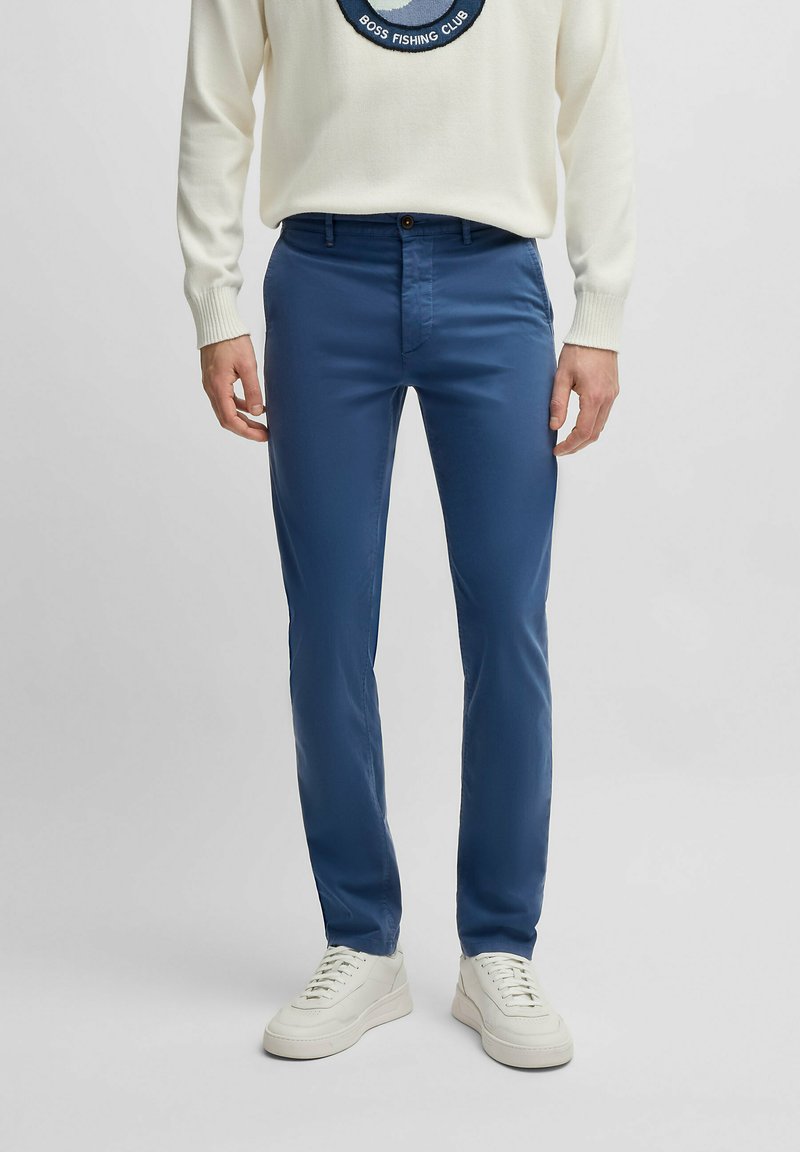 Niebieskie bawełniane spodnie o slim fit. Posiadają zapięcie na guzik z przodu i kieszenie boczne. Noszone z białym swetrem w wzory i trampkami.