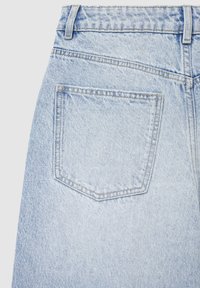 Jeans en denim bleu clair avec une poche arrière ornée de détails de couture. Le tissu présente une texture douce avec une apparence délavée et usée.