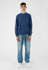 Niebieski sweter z długim rękawem, wykonany z miękkiego materiału, w połączeniu z jasnoniebieskimi dżinsami i białymi trampkami. Prosty, luźny fason.