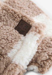 Tissu sherpa doux beige et blanc avec une étiquette foncée indiquant "HERE COMES THE STAR", cousue dans le matériau duveteux.