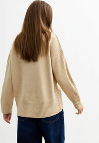 Suéter de punto beige con dobladillo y mangas rayadas texturizadas, que presenta un ajuste holgado y un diseño de corte ancho. Combinado con jeans de mezclilla oscuros.