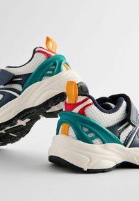 Buty sportowe z białą siateczkową cholewką, granatowymi akcentami i teksturowaną czarną podeszwą. Posiadają kolorowe akcenty w odcieniach turkusu, czerwieni i pomarańczy.