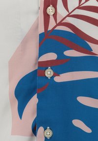 Gestructuurde stoffen shirt met een blauw en roze bladerenpatroon met beige accenten; heeft vijf ronde plastic knopen langs de opening.