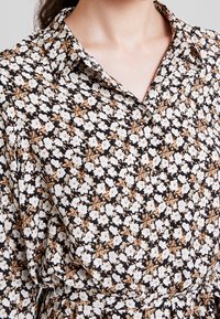 Blommig klänning med svart bakgrund och vita och bruna blommor, en knapp-down krage, samt mjukt tyg med en avslappnad passform.