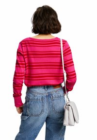 Gekürzter rosa-rot gestreifter Pullover mit gerippten Bündchen, kombiniert mit hoch taillierter Jeans und einer hellgrauen Schultertasche.
