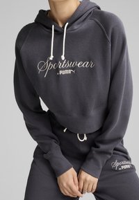 Sweat à capuche gris foncé avec cordons blancs et texte brodé "Sportswear by PUMA". Texture douce, coupe courte, poignets et taille côtelés.