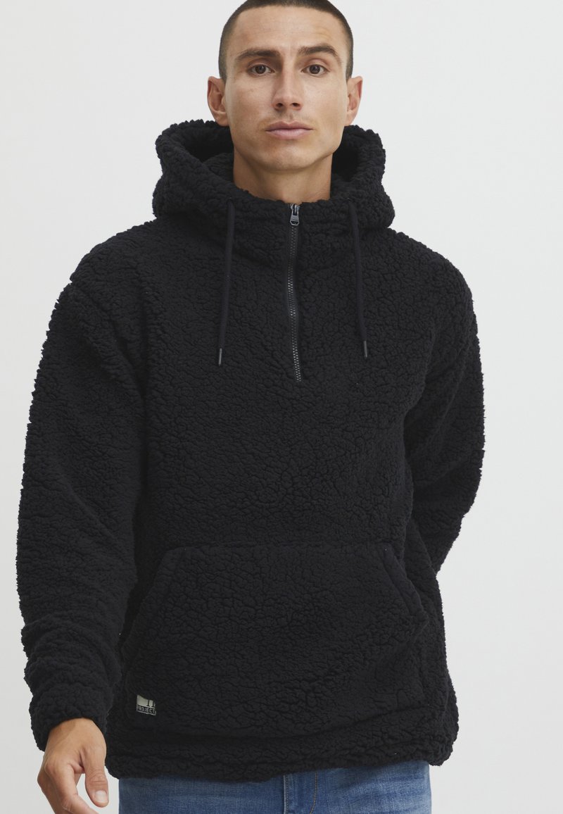 Svart fleece hettegenser med kvart glidelås, hette og frontkangaroo-lomme. Strukturert, plysj stoff med justerbare snor for hetten.