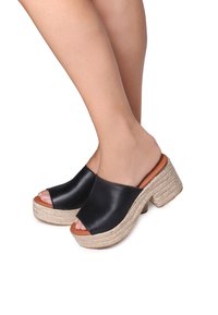 Black leather platform mules with an open toe, showcasing a woven jute heel and a smooth, rounded upper design.