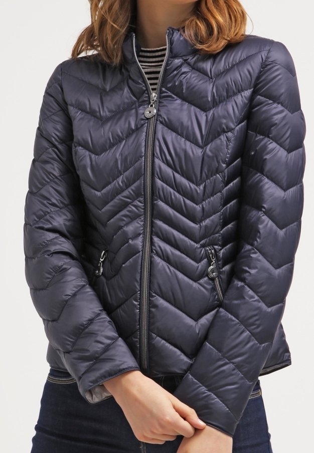 Veste matelassée bleu marine avec piqûres en forme de chevrons, fermeture éclair à l'avant et poches latérales. Dotée d'un col montant et d'une texture douce et lisse.