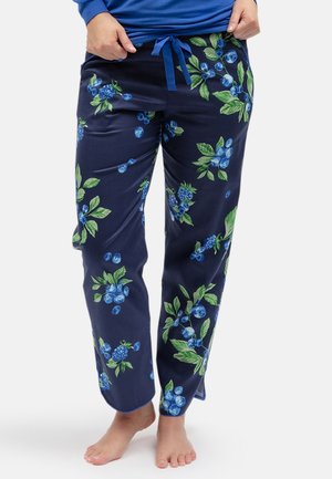 Person trägt marineblaue Pyjamahose mit blau-grünem Blumenmuster, barfuß, zieht den Bund mit den Händen leicht hoch.