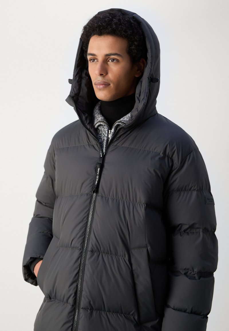 Chaqueta acolchada negra con cierre frontal, diseño sin características destacadas y capucha. Fabricada en un material suave, aislante y con textura acolchada.