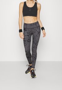 Sports bra in black, high-waisted leggings with gray and black marble pattern, and black athletic shoes with red and yellow accents.