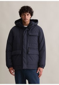Granatowa ocieplana kurtka z kapturem, wyposażona w liczne kieszenie, elastyczne mankiety i teksturowaną powierzchnię dla dodatkowego ciepła.
