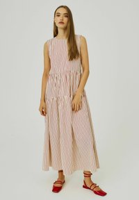Abito senza maniche, lungo fino al pavimento, color crema con strisce verticali rosse; vita arricciata, gonna fluente, abbinato a scarpe basse rosse con cinturini.