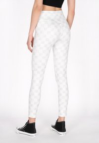 Witte legging met een ruitpatroon van rekbaar materiaal, met een hoge tailleband en een slim fit, gecombineerd met zwarte high-top sneakers.
