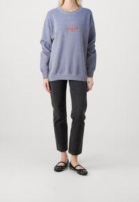 Ljuslila sweatshirt med röd "VISIONS" logotyp, ihop med svarta jeans och svarta ballerina-skor med vita nitar. Avslappnad passform, mjuk textur.