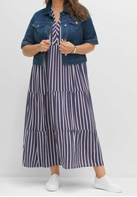 Jeansjacka med korta ärmar över en marinblå maxiklänning med vertikala röda och vita ränder och en flerstegsdesign. Vita sneakers.